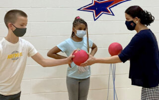 Teacher handing sports balls to two students in a gym