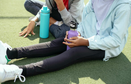 Two girls sitting on athletic field with water bottles